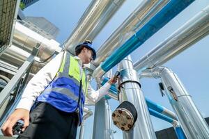Industrial engineer adjusting pipeline valve with radio communication on construction site. Engineer on urban construction site using radio to coordinate with team on a sunny industrial rooftop. photo