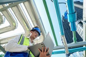 Industrial engineer adjusting pipeline valve with radio communication on construction site. Engineer on urban construction site using radio to coordinate with team on a sunny industrial rooftop. photo