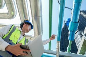 Industrial engineer adjusting pipeline valve with radio communication on construction site. Engineer on urban construction site using radio to coordinate with team on a sunny industrial rooftop. photo