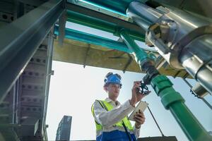 Male engineer monitoring machinery on a rooftop with city skyline in the background, wearing safety gear photo