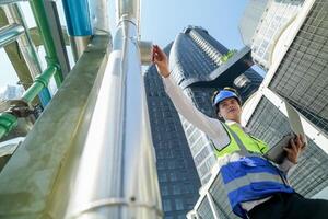 Industrial engineer adjusting pipeline valve with radio communication on construction site. Engineer on urban construction site using radio to coordinate with team on a sunny industrial rooftop. photo