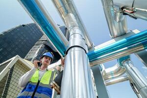 Industrial engineer adjusting pipeline valve with radio communication on construction site. Engineer on urban construction site using radio to coordinate with team on a sunny industrial rooftop. photo