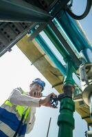 Industrial engineer adjusting pipeline valve with radio communication on construction site. Construction worker using walkie-talkie to coordinate machinery adjustments on a sunny day. photo