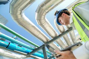 Industrial engineer adjusting pipeline valve with radio communication on construction site. Engineer on urban construction site using radio to coordinate with team on a sunny industrial rooftop. photo