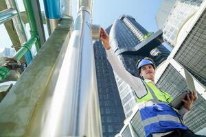 Industrial engineer adjusting pipeline valve with radio communication on construction site. Engineer on urban construction site using radio to coordinate with team on a sunny industrial rooftop. photo