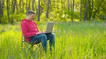 Man working on laptop in summer forest At The Sunny Day. Busy freelance worker is tired and wants to rest. Freelancer Remote Work Concept. 4K video