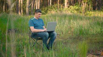 Man working on laptop in summer forest At The Sunny Day. Busy worker freelancer working on modern tech notebook device. Remote Work Concept. 4K video
