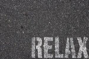 Road asphalt texture. Bitumen structure with painted relax word. photo