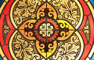 An antique cross is made of a stained glass window and is decorated with floral and geometric ornaments. photo