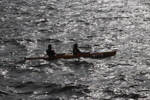 Two people go on a kayak along the bay in the reflection of sun glare on the water. photo