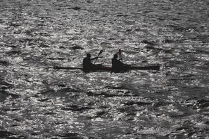 Two people go on a kayak along the bay in the reflection of sun glare on the water. photo