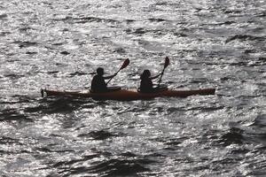Two people go on a kayak along the bay in the reflection of sun glare on the water. photo