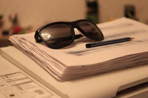 Sunglasses with pen lie on a stack of paper on the printer photo
