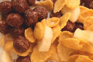 Cornflakes with chocolate balls sliced banana and milk. Filling background. Macro close-up. photo