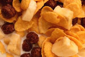 Cornflakes with chocolate balls sliced banana and milk. Filling background. Macro close-up. photo