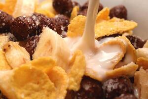 Cornflakes with chocolate balls sliced banana and stream of milk. Filling background. Macro close-up. photo