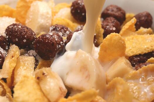 Cornflakes with chocolate balls sliced banana and stream of milk. Filling background. Macro close-up. photo