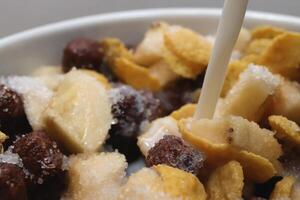 Cornflakes with chocolate balls sliced banana and stream of milk. Filling background. Macro close-up. photo