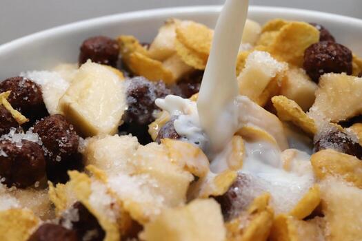 Cornflakes with chocolate balls sliced banana and stream of milk. Filling background. Macro close-up. photo