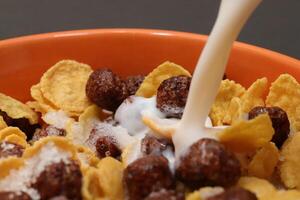 Cornflakes with chocolate balls sliced banana and stream of milk. Filling background. Macro close-up. photo