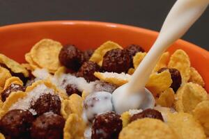 Cornflakes with chocolate balls sliced banana and stream of milk. Filling background. Macro close-up. photo