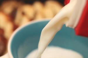A stream of milk pours into a mug with sweet swirling roll bun slices on background. Macro closeup. photo