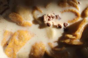Cornflakes with chocolate sliced banana and milk in sun light. Filling background. Macro close-up. photo