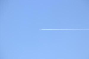 The plane flies in the clear sky, leaving a trail in a long line. photo