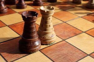 Black and white rooks stand on a chessboard with figures on background. Wood game chessboard. photo