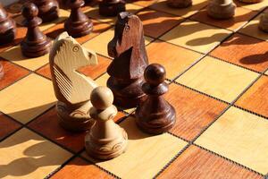 Black and white pawn and horses stand on a chessboard with figures on background. Wood game chessboard. photo