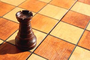 One black rook figure stands on a chess board. Wood game chessboard background. photo