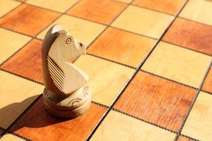 The figure of a white horse stands on a chess board. Wood game chessboard background. photo