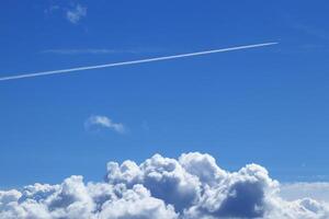 The trail of a flying airplane in a clear blue sky over large clouds. photo