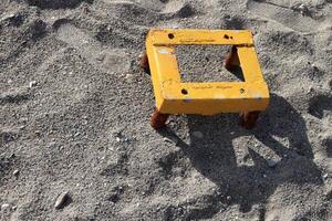 Yellow metal construction with rusty legs. Metal stool on the sand texture. Summer beach background. photo