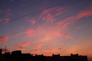 Pink blue sky at sunrise against the background of the silhouette of the roofs of the city buildings and wired in the sky. Morning city skyline landscape. photo