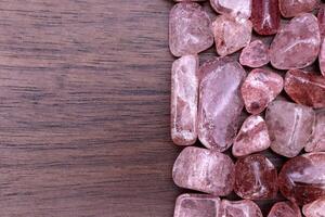 Strawberry quartz heap jewel stones texture on half brown varnished wood background. Place for text. photo