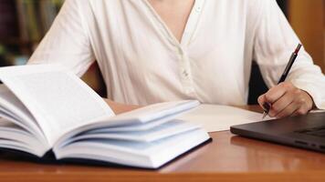 onherkenbaar meisje leerling Holding boek, maken aantekeningen Bij de tafel, bureau in modern Universiteit campus bibliotheek. onderwijs concept, kennis, wijsheid, afstuderen video