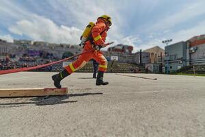 In a dynamic display of synchronized teamwork, firefighters hustle to carry, connect, and deploy firefighting hoses with precision, showcasing their intensive training and readiness for challenging photo