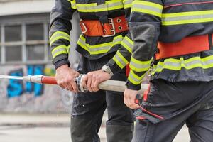 In a dynamic display of synchronized teamwork, firefighters hustle to carry, connect, and deploy firefighting hoses with precision, showcasing their intensive training and readiness for challenging photo