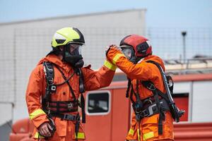 A unified team of firefighters, adorned in their uniforms, engages in a heartfelt celebration marked by triumphant salutes and cheers, embodying the joy and gratitude following the successful photo