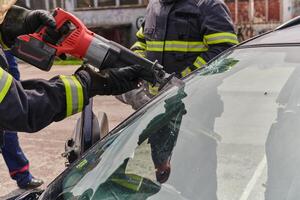 un dedicado equipo de profesional bomberos emplea especializado herramientas a cortar y descanso mediante vehículo destrucción, exhibiendo su experto colaboración y rápido respuesta en rescatar individuos foto