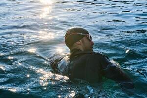 Triathlon athlete swimming on lake in sunrise wearing wetsuit photo