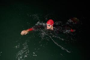 A determined professional triathlete undergoes rigorous night time training in cold waters, showcasing dedication and resilience in preparation for an upcoming triathlon swim competition photo