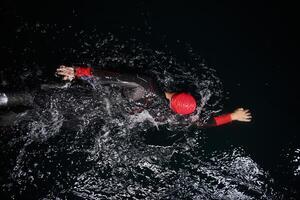 A determined professional triathlete undergoes rigorous night time training in cold waters, showcasing dedication and resilience in preparation for an upcoming triathlon swim competition photo