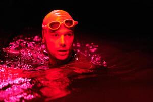 authentic triathlete swimmer having a break during hard training on night neon gel light photo