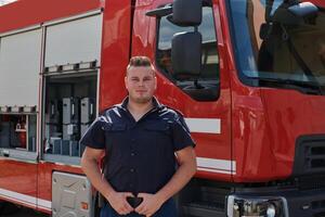 A confident firefighter strikes a pose in front of a modern firetruck, exuding pride, strength, and preparedness for emergency response photo