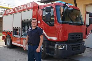 A confident firefighter strikes a pose in front of a modern firetruck, exuding pride, strength, and preparedness for emergency response photo