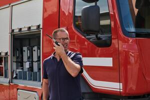 A dedicated firefighter, captured in a moment of communication, stands before a modern firetruck, showcasing the seamless integration of technology in emergency response photo
