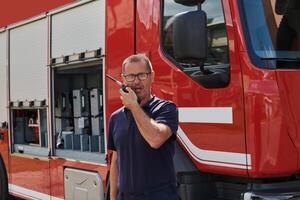 A dedicated firefighter, captured in a moment of communication, stands before a modern firetruck, showcasing the seamless integration of technology in emergency response photo