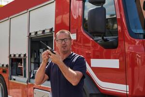 A dedicated firefighter, captured in a moment of communication, stands before a modern firetruck, showcasing the seamless integration of technology in emergency response photo